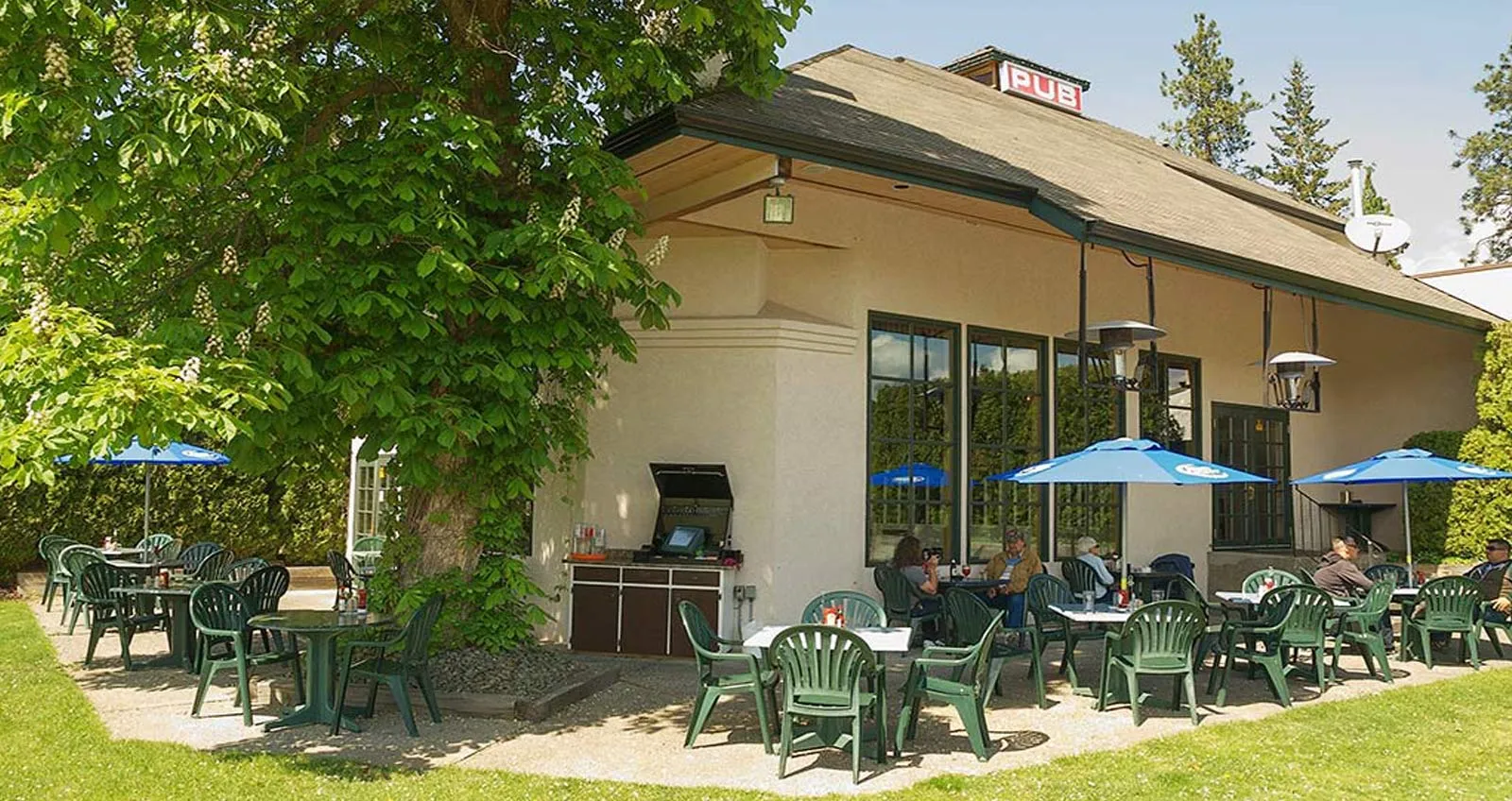 Shaded patio tables beneath leafy trees at McCulloch Station Pub with guests enjoying a summer afternoon